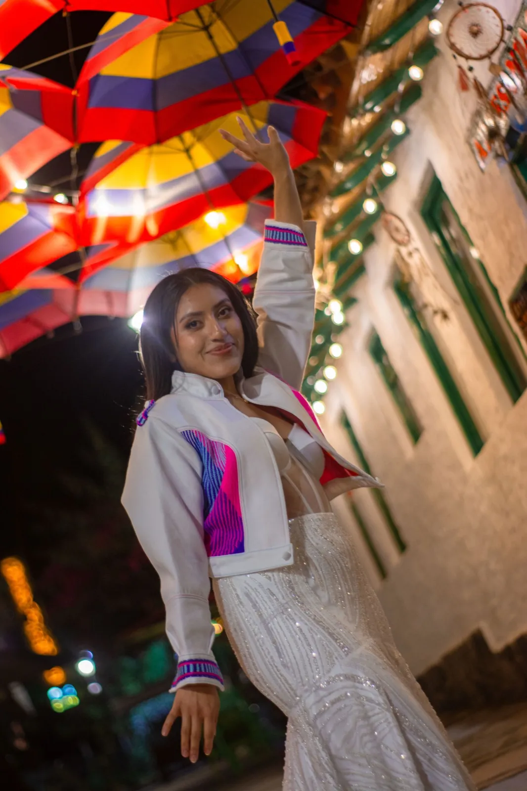 Mujer con chaqueta blanca de detalles rosa y azul bajo sombrillas de colores